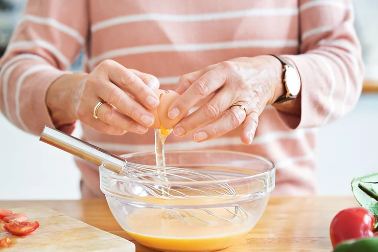 woman cracking an eggs into a clear bowl with a whisk