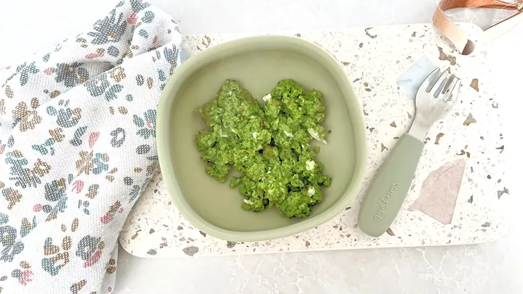 Green eggs no ham in greeen silicone suction bowl with baby fork on a terrazzo board - Starting Solids Australia recipe.