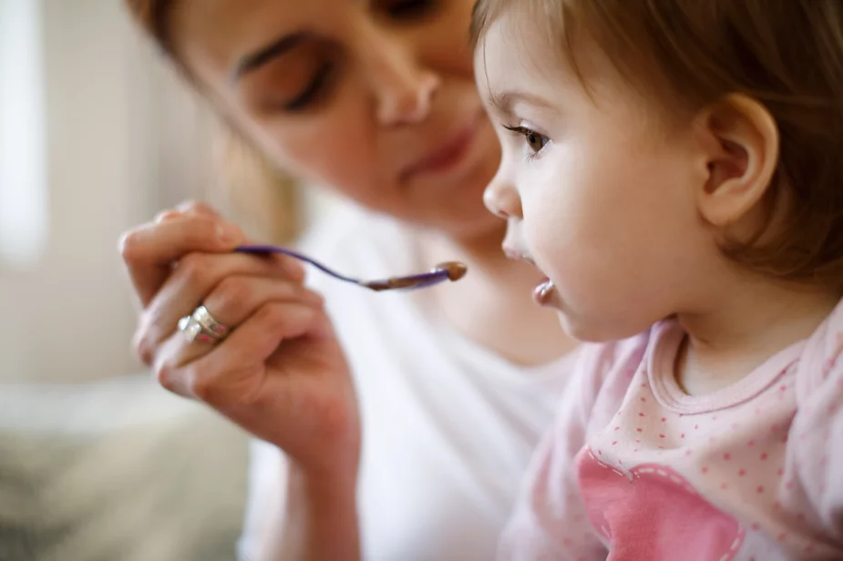 Toddler girl being spoon fed by woman