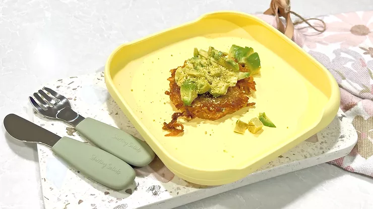 Potato and Carrot Rostis in a yellow silicone suctio plate on a terrazzo board with baby cutlery - Starting Solids Australia recipe.