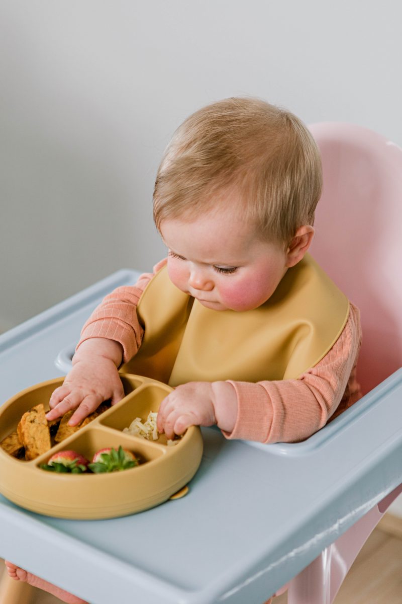 Baby in highchair wearing Starting Solids Australia Silly Bib, eating food from a Suckie Scoop Divided Plate in Biscoff colour.