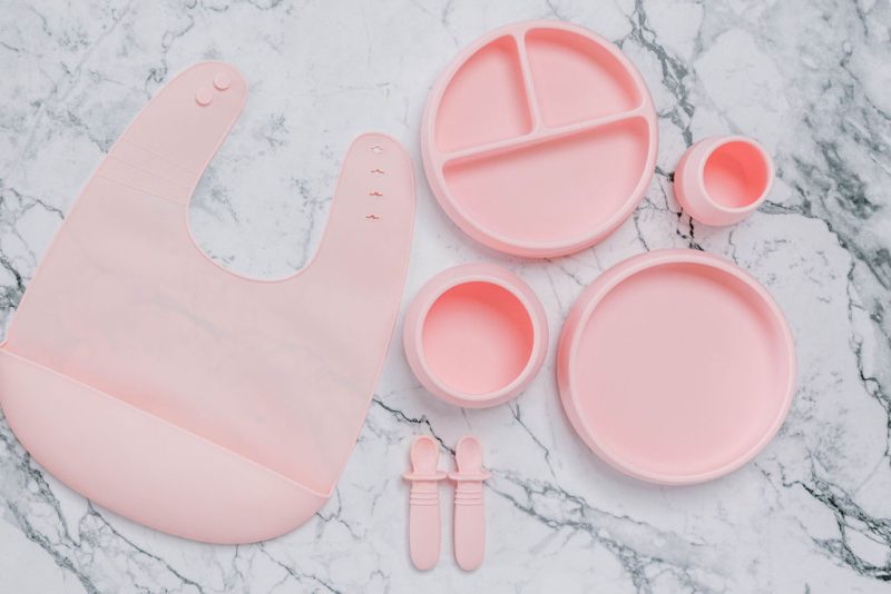 Pink silicone bib, Bubbie Cup, Suckie Scoop Divided Plate, Suckie Scoop Plate, Suckie Scoop Bowl and Selfie Spoon set for babies by Starting Solids Australia, on a marble bench.