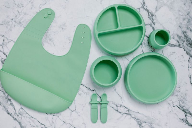 Green silicone bib, Bubbie Cup, Suckie Scoop Divided Plate, Suckie Scoop Plate, Suckie Scoop Bowl and Selfie Spoon set for babies by Starting Solids Australia, on a marble bench.