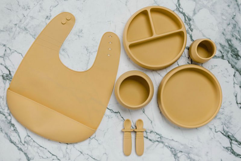 Yellow silicone bib, Bubbie Cup, Suckie Scoop Divided Plate, Suckie Scoop Plate, Suckie Scoop Bowl and Selfie Spoon set for babies by Starting Solids Australia, on a marble bench.