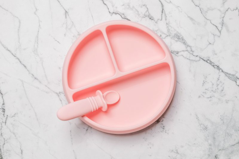 Light pink Suckie Scoop Divided Plate with Selfie Spoon by Starting Solids Australia, on a marble bench.