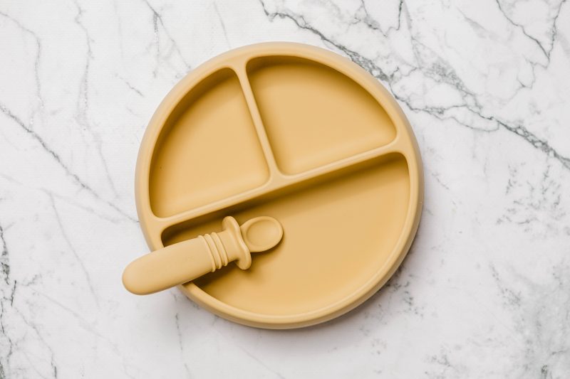 Yellow Suckie Scoop Divided Plate with Selfie Spoon by Starting Solids Australia, on a marble bench.