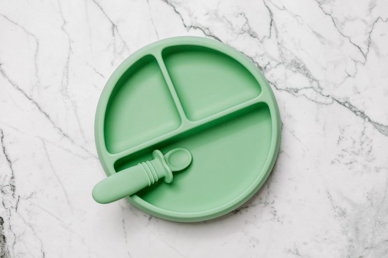 Green Suckie Scoop Divided Plate with Selfie Spoon by Starting Solids Australia, on a marble bench.