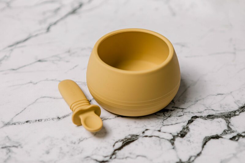 Suckie Scoop Bowl with Selfie Spoon in 'Biscoff' Yellow by Starting Solids Australia, on a marble bench.