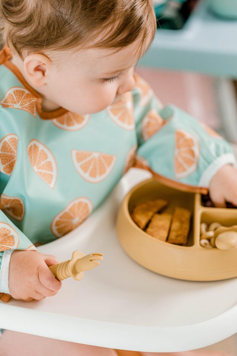 Baby eating solid foods from Suckie Scoop Divided Plate with Selfie Fork and wearing a Smockie Bib by Starting Solids Australia.