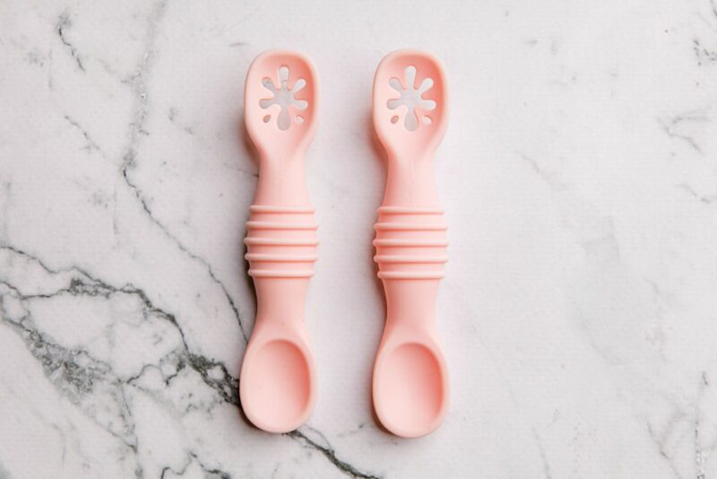 Pink silicone sticky spoons for baby on a marble bench by Starting Solids Australia