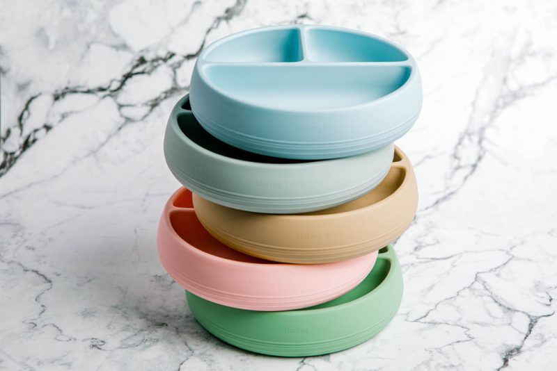 Stack of Suckie Scoop Divided Plates in assorted colours by Starting Solids Australia on a marble bench.