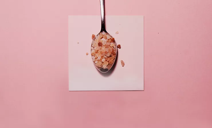 Pink himalayan rock salt on a silver spoon on a pink background.