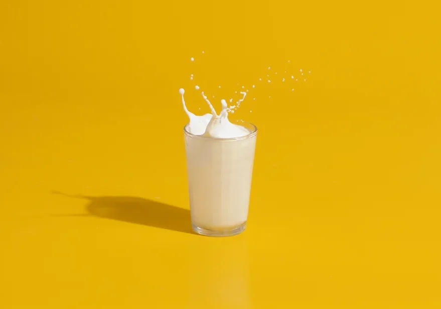 Milk splashing out the top of a glass against a yellow background