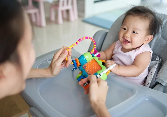 Adult playing with baby in highchair with sensory toy.