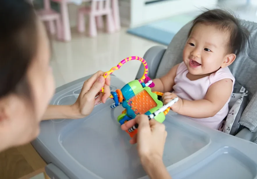 Baby in highchair playing with sensory toy with parent