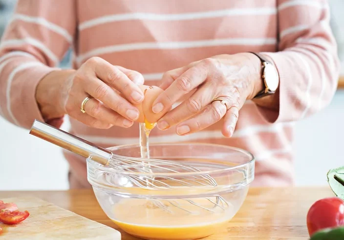 woman cracking an eggs into a clear bowl with a whisk