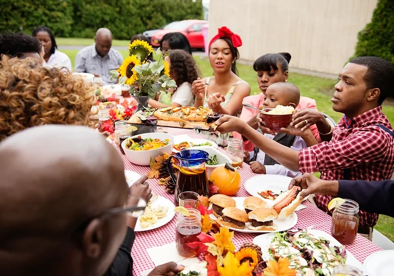 African diaspora family mealtime outdoors around a long table.