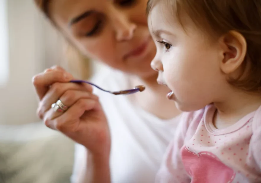 Toddler girl being spoon fed by woman