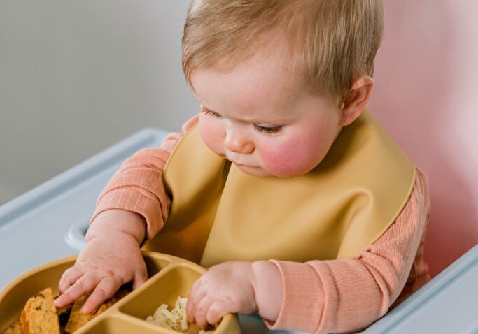 Baby eating solid food from Starting Solids Australia's silicone suction plate and catch-all bib.