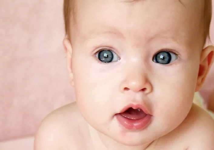 Blue eyed baby (face detail) with a pink background