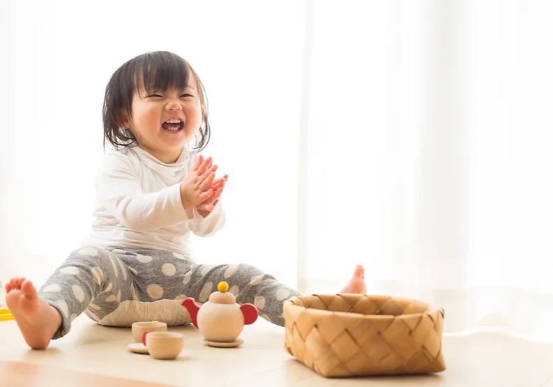 Asian baby sitting on the floor with play tea set and woven basket