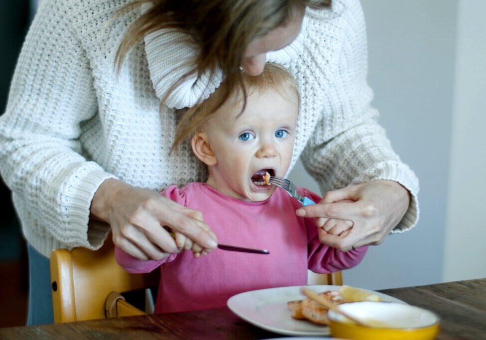 a mother teaching a baby to use cutlery