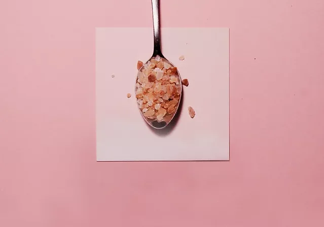 Pink himalayan rock salt on a silver spoon on a pink background.